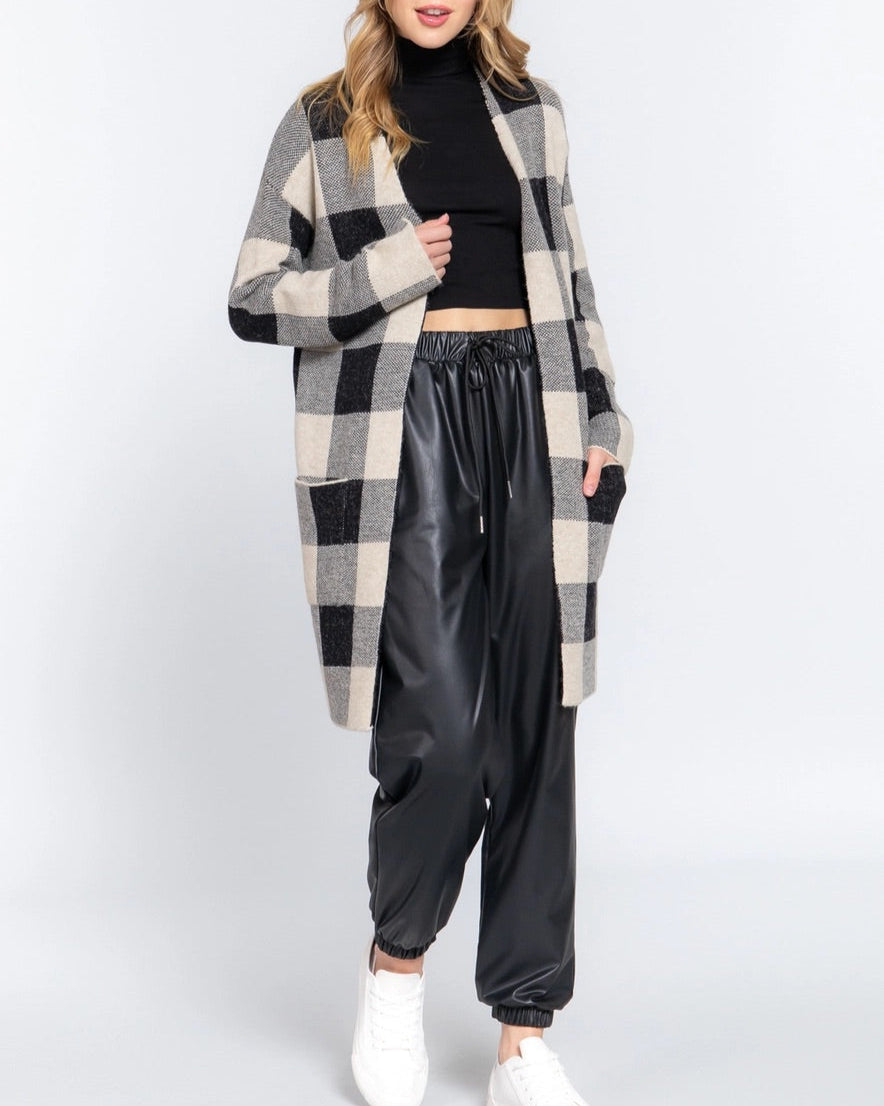 Woman wearing a checkered cardigan, black turtleneck, and black pants on a white background.