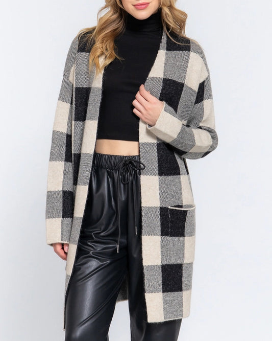 Woman wearing a checkered cardigan over a black top and leather pants on a white background.