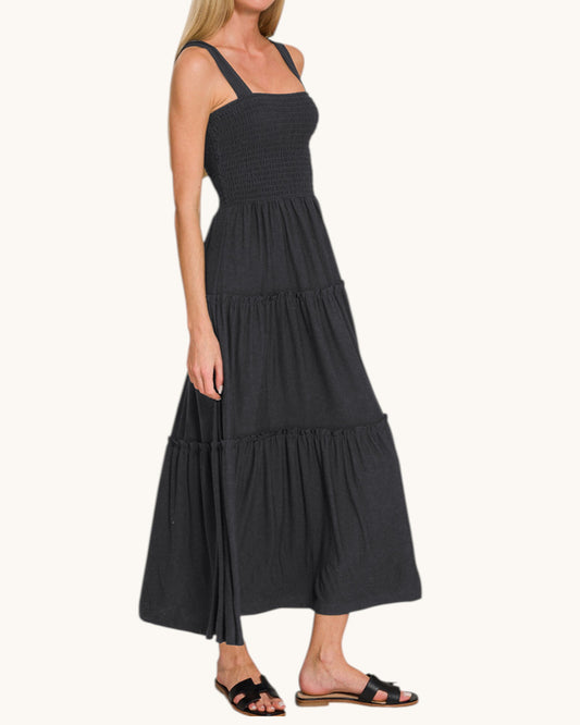 Woman wearing a black sleeveless dress with tiered layers on a white background.