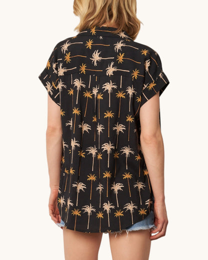 Back view of a person wearing a black shirt with palm tree pattern on a white background.