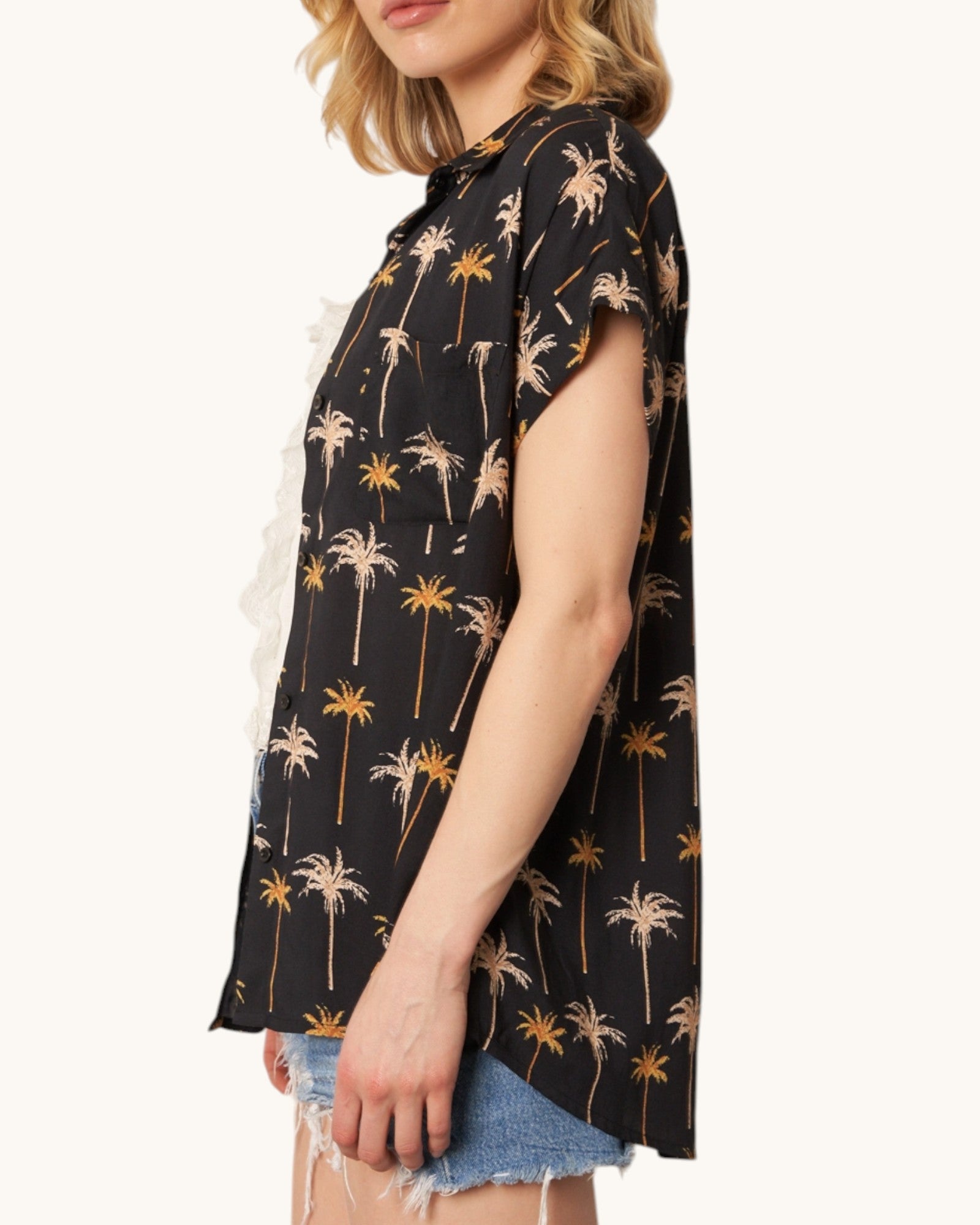 Side view of a black shirt with palm tree pattern worn by a person on a white background.
