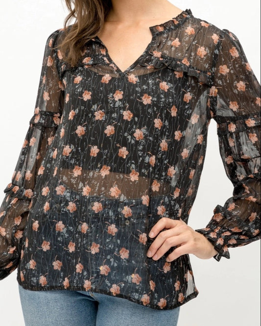 Woman wearing a black semi-sheer floral blouse with a white background. 