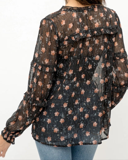Woman wearing a black semi-sheer floral blouse with a white background. 