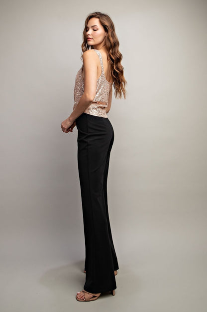 Woman wearing a sparkly top and black pants on a plain background