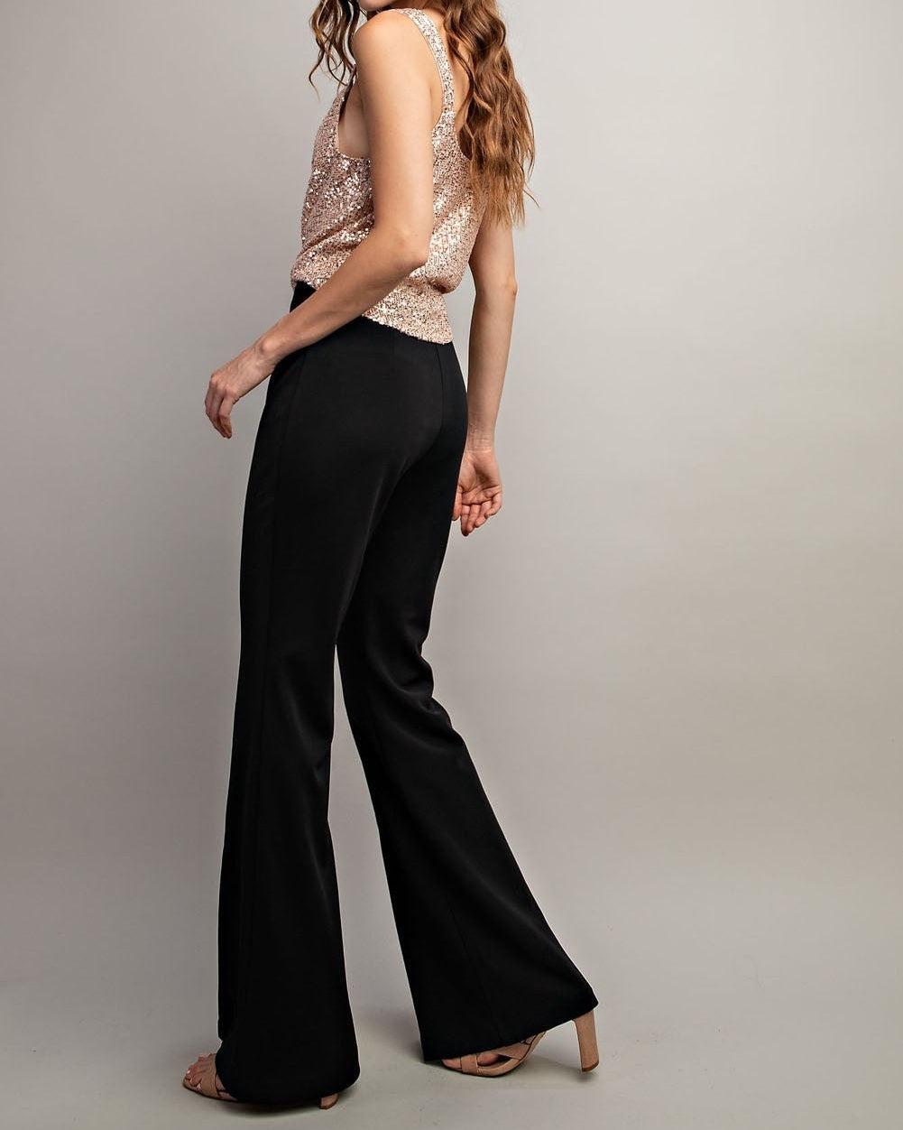 Woman wearing a sparkly top and black flared pants on a plain background.
