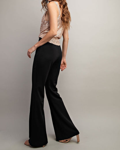 Woman wearing a sparkly top and black flared pants on a plain background.