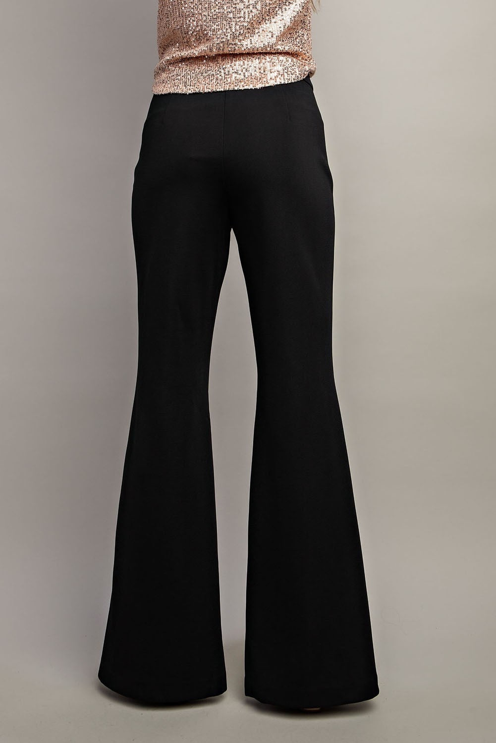 Black flared pants worn with a rose gold sequin top on a neutral background.