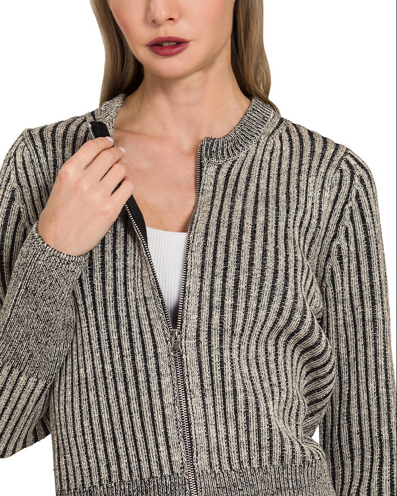 Woman wearing a charcoal ribbed knit zip up cardigan over a white top and blue jeans on a white background.