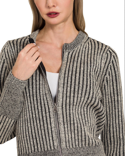 Woman wearing a charcoal ribbed knit zip up cardigan over a white top and blue jeans on a white background.