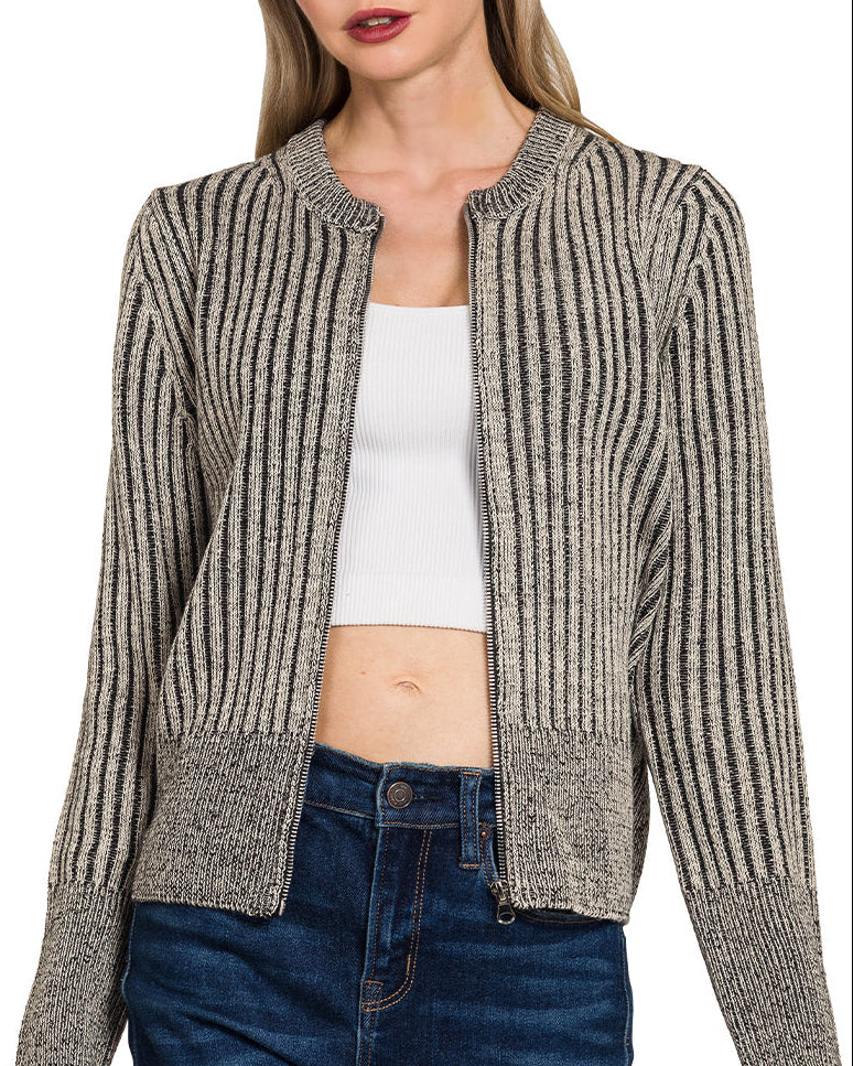 Woman wearing a charcoal ribbed knit zip up cardigan over a white top and blue jeans on a white background.