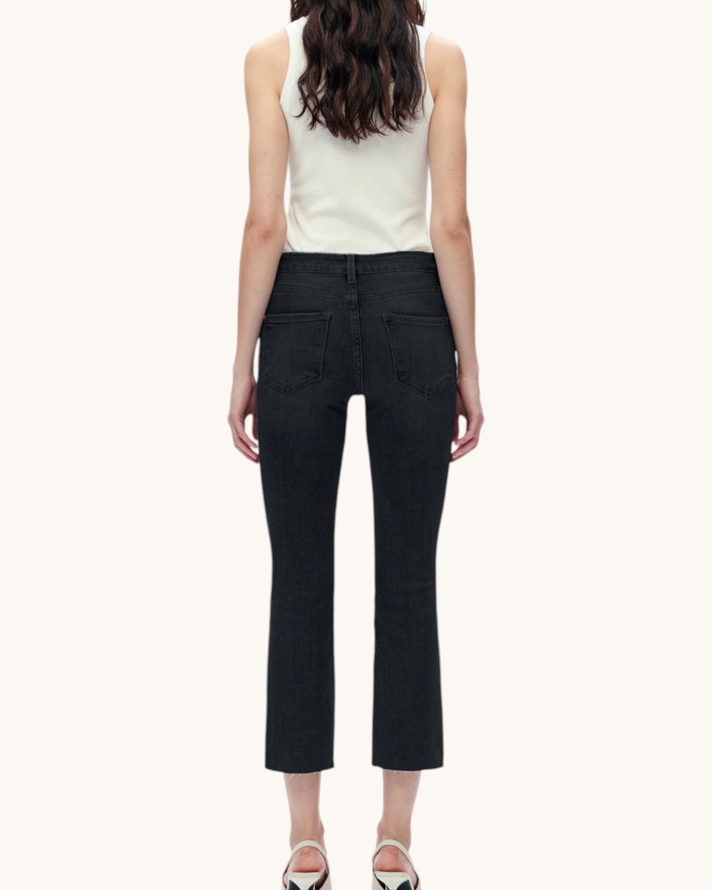 Person wearing a white sleeveless top and black pants on a white background.