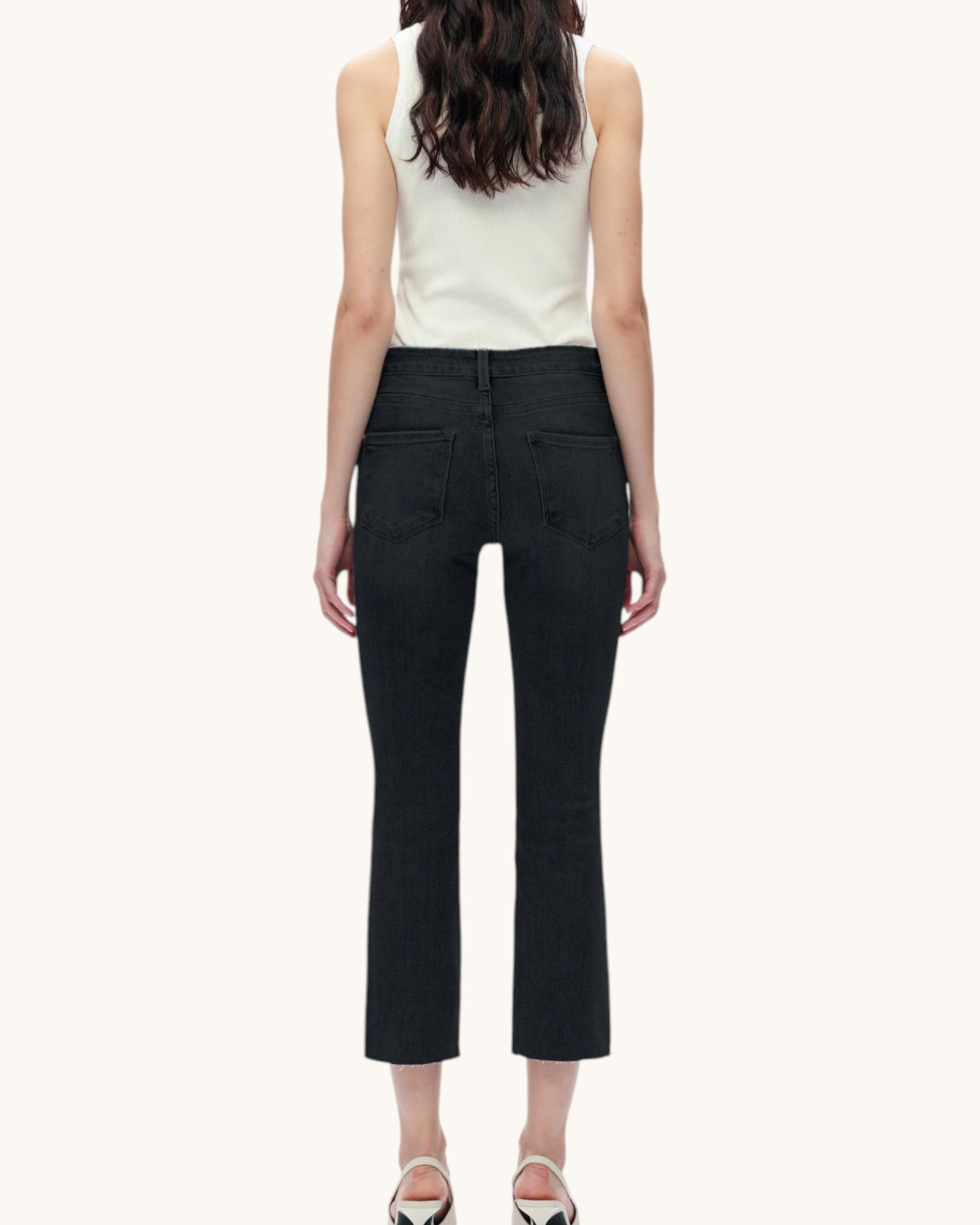 Person wearing a white sleeveless top and black pants on a white background.