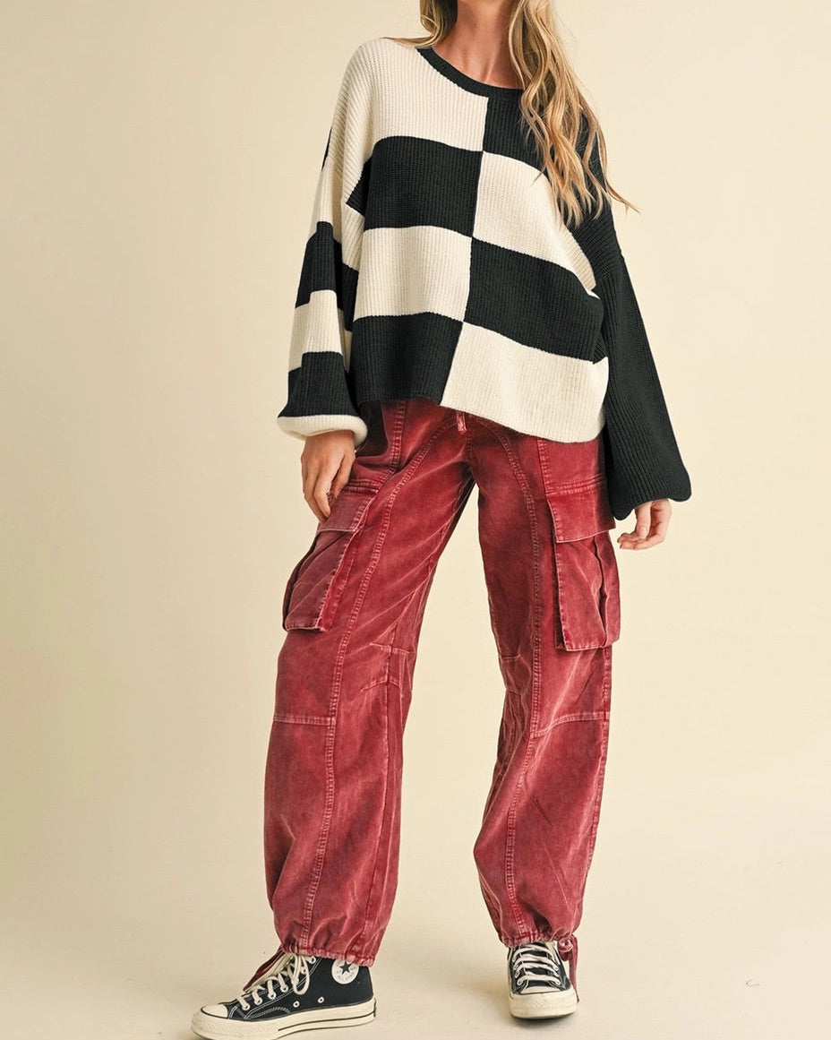 Woman wearing a black and white checkered sweater and red pants on a beige background