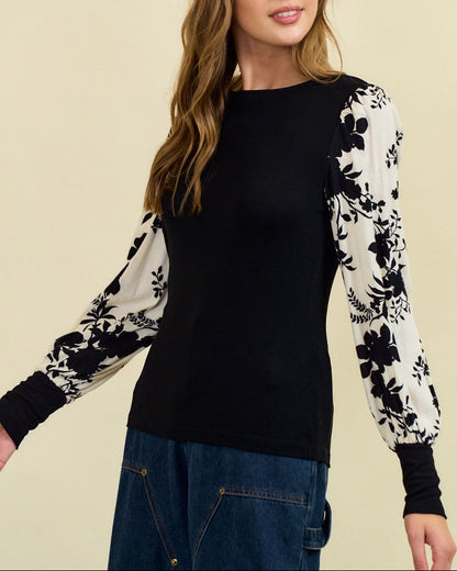 Woman wearing a black top with floral sleeves against a beige background.