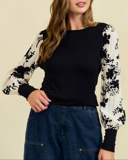 Woman wearing a black top with floral sleeves against a beige background