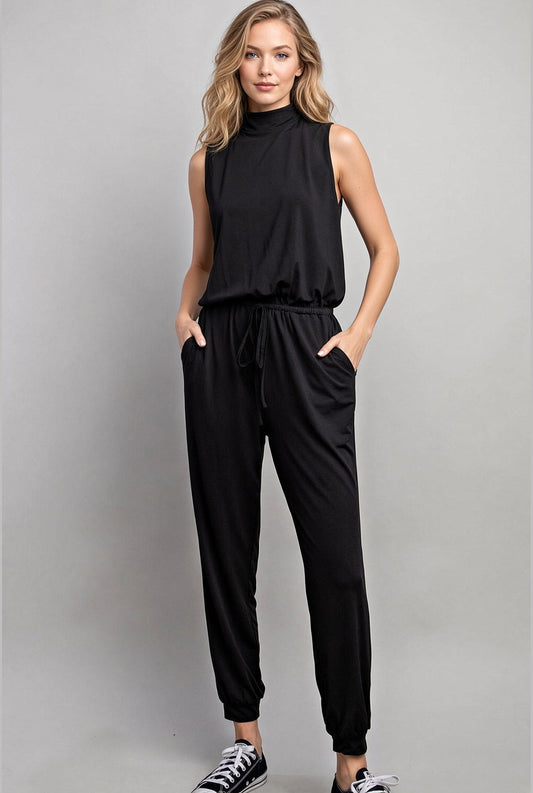 Woman wearing a silky sleeveless black mock neck jumpsuit and black sneakers.