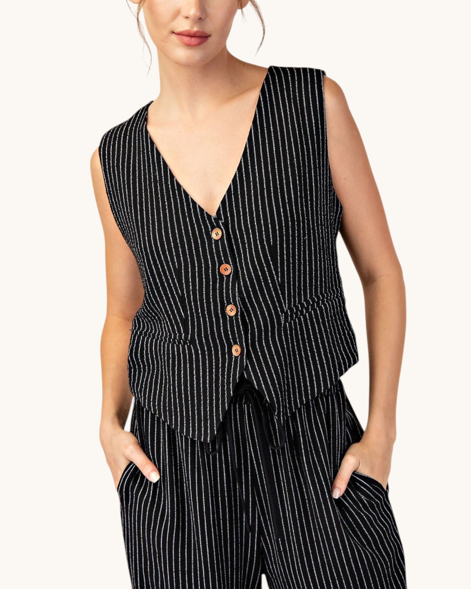 Woman wearing a fitted black pinstripe sleeveless button up vest and matching pants. 