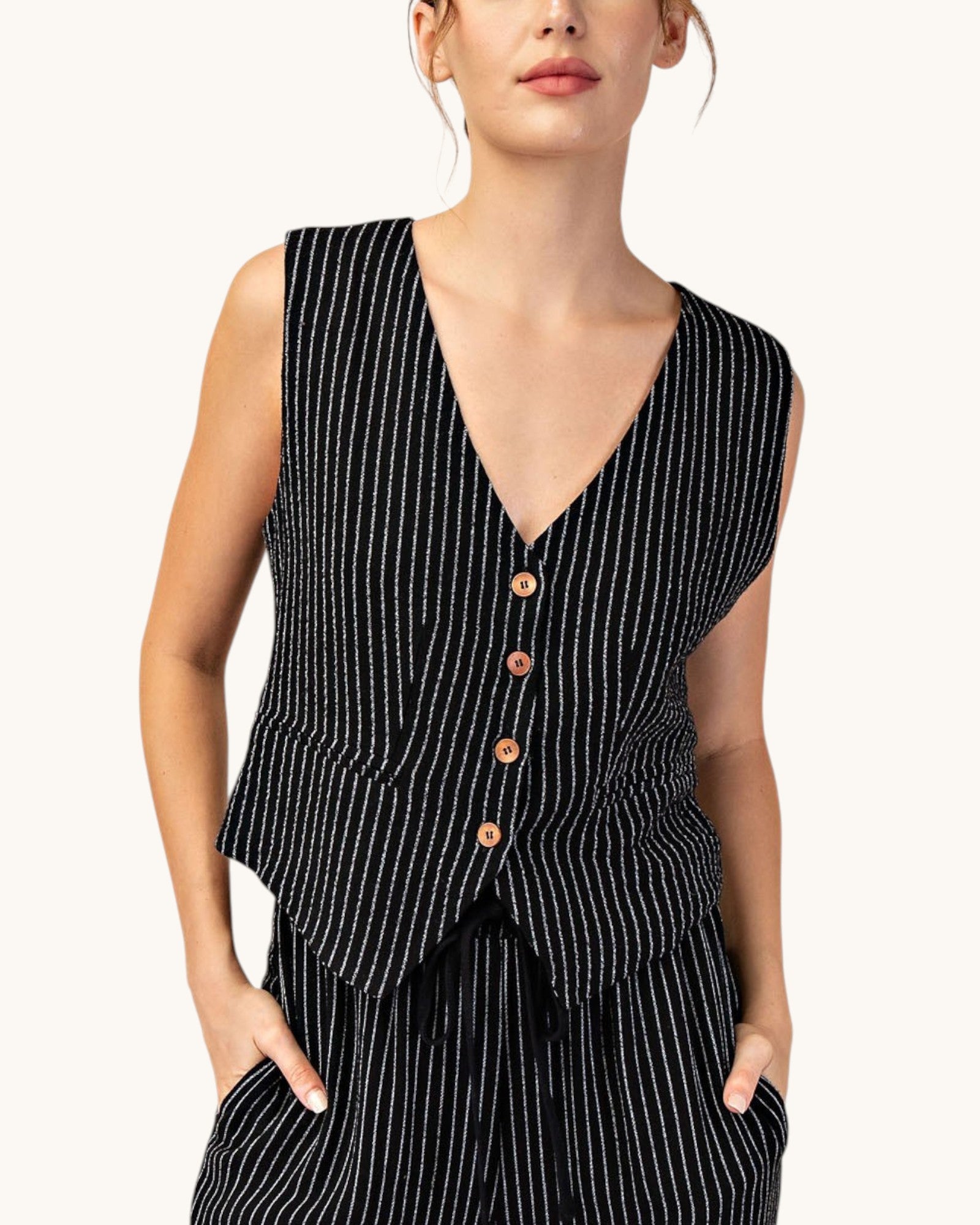 Woman wearing a cropped, fitted black pinstripe sleeveless button up vest and matching pants. 
