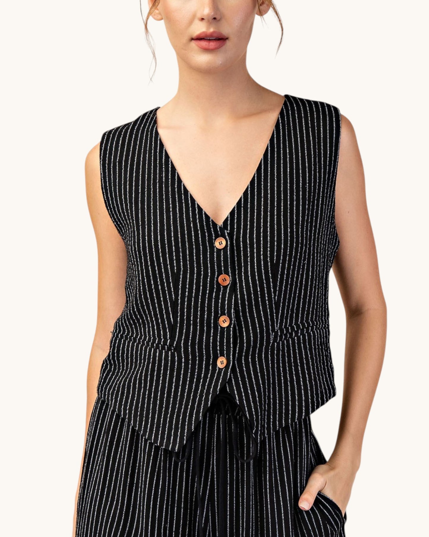A sleeveless black vest with thin white vertical pinstripes and four brown buttons, worn by a model against a plain off-white background.