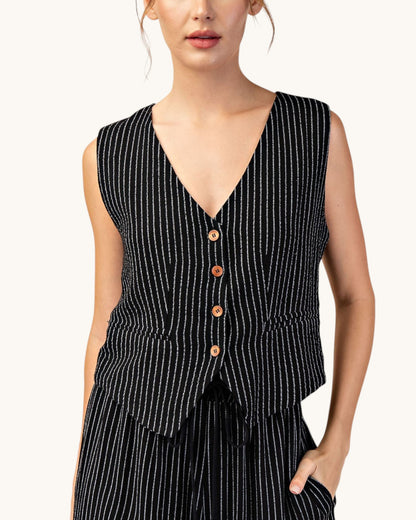 A sleeveless black vest with thin white vertical pinstripes and four brown buttons, worn by a model against a plain off-white background.