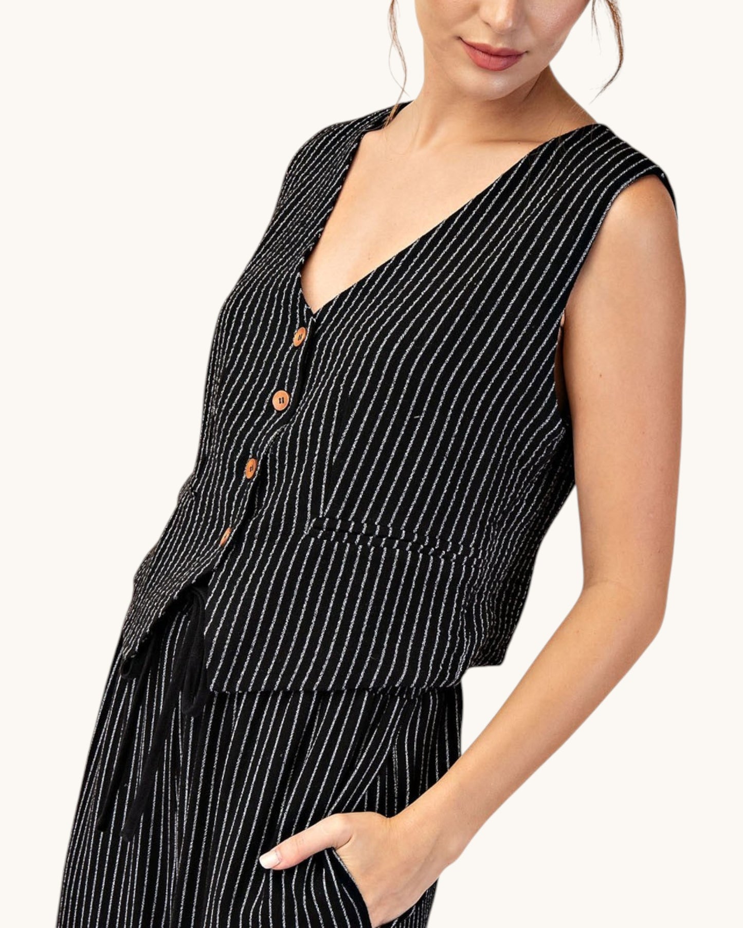 Side view of a woman wearing a cropped, fitted black pinstripe sleeveless button up vest and matching pants. 