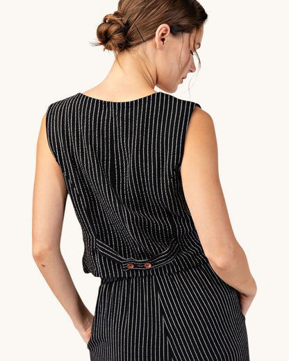 Back view of a woman wearing a cropped, fitted black pinstripe sleeveless button up vest and matching pants. 