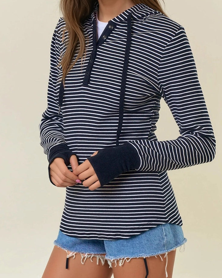 Woman wearing a black and white striped henley hoodie with denim shorts on a beige background. 