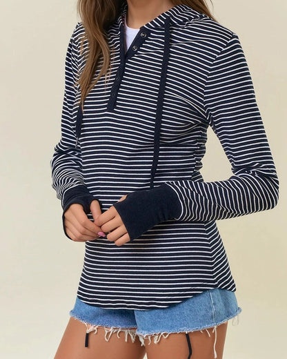 Woman wearing a black and white striped henley hoodie with denim shorts on a beige background. 
