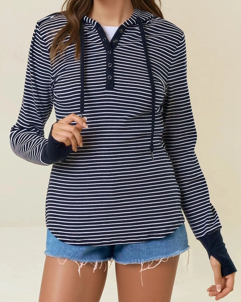 Woman wearing a black and white striped henley hoodie with denim shorts on a beige background. 