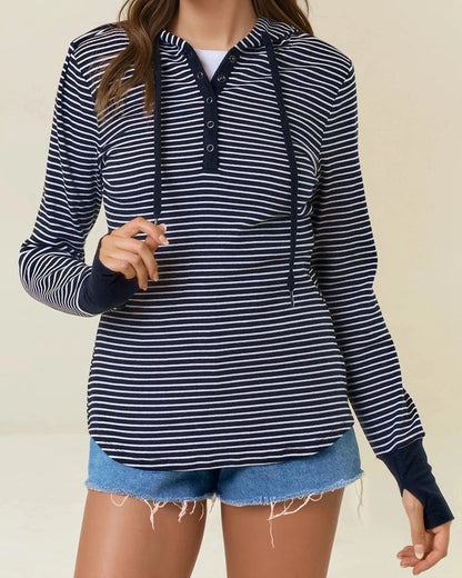 Woman wearing a black and white striped henley hoodie with denim shorts on a beige background. 