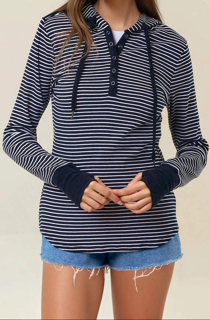 Woman wearing a black and white striped henley hoodie with denim shorts on a beige background. 
