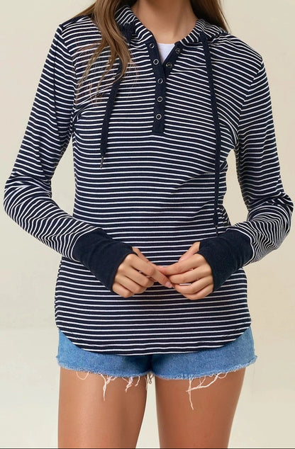 Woman wearing a black and white striped henley hoodie with denim shorts on a beige background. 