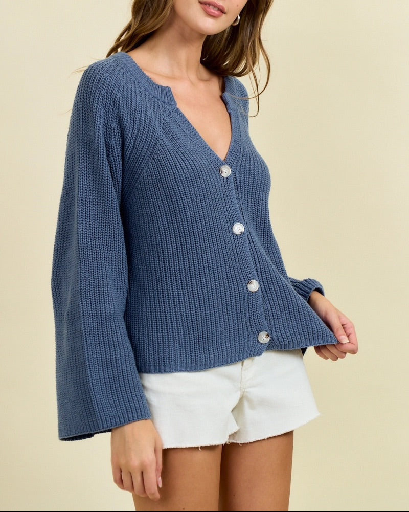 Woman wearing a blue cardigan over a white top against a beige background.