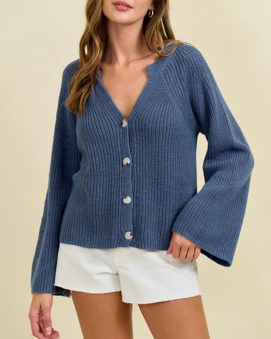 Woman wearing a blue ribbed cardigan over white shorts on a beige background