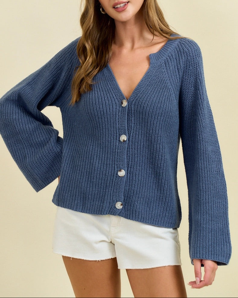 Woman wearing a blue knitted cardigan over white shorts on a beige background