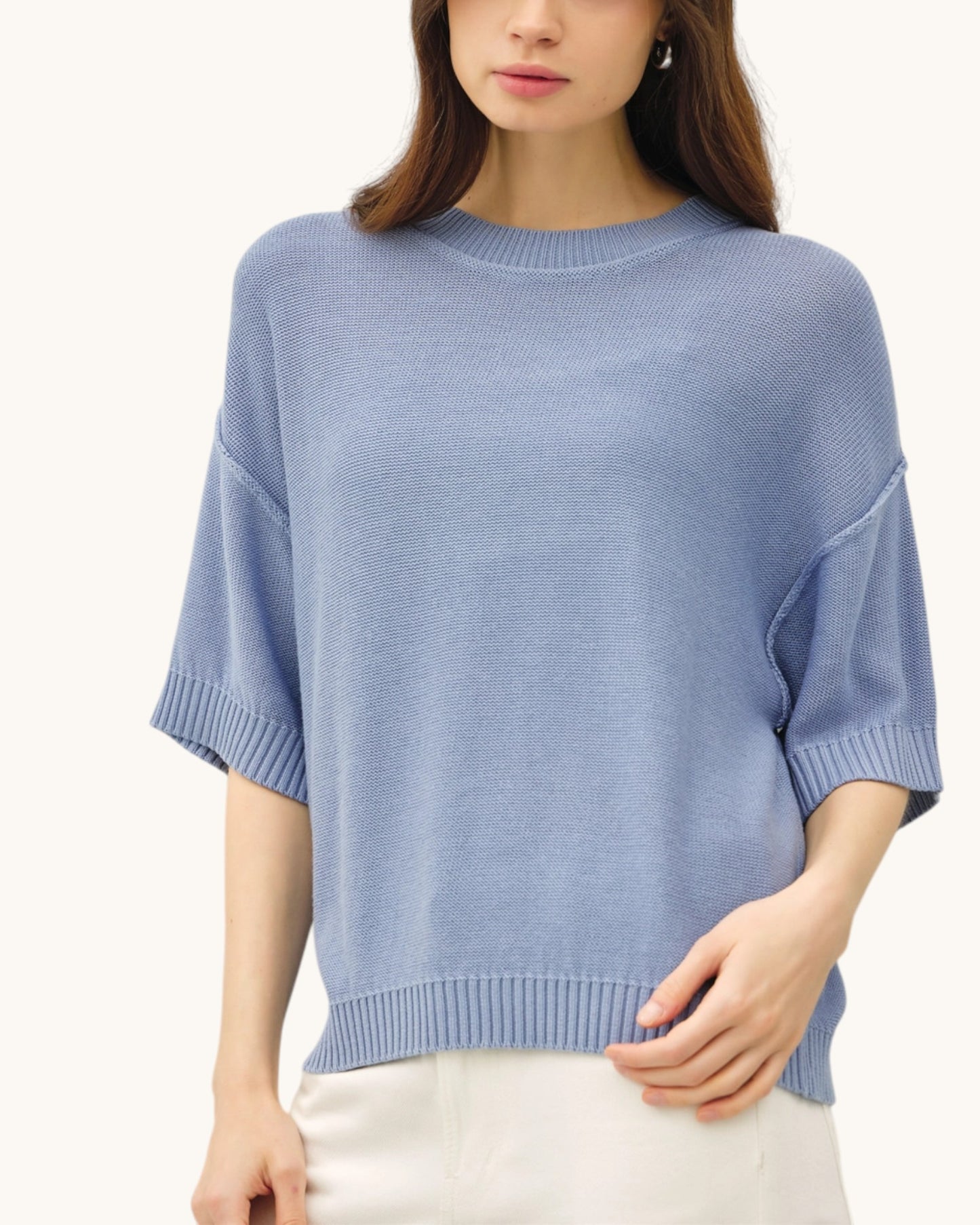 Woman wearing a light blue relaxed fit short sleeve sweater against a white background.