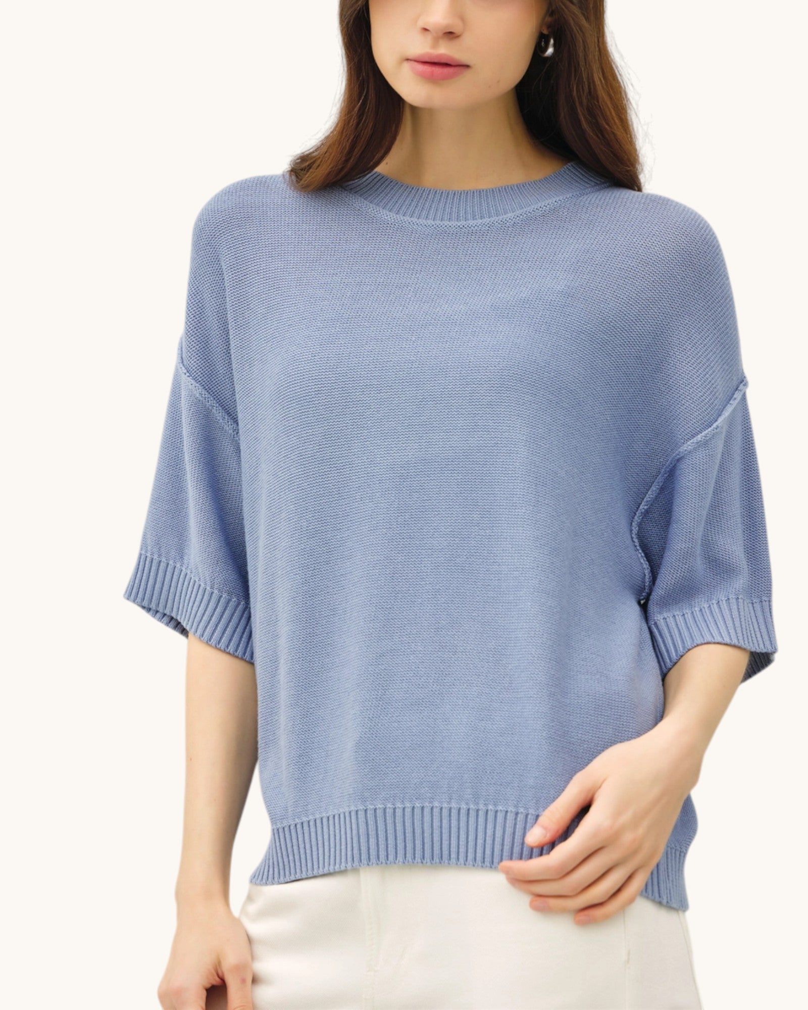 Woman wearing a light blue relaxed fit short sleeve sweater against a white background.