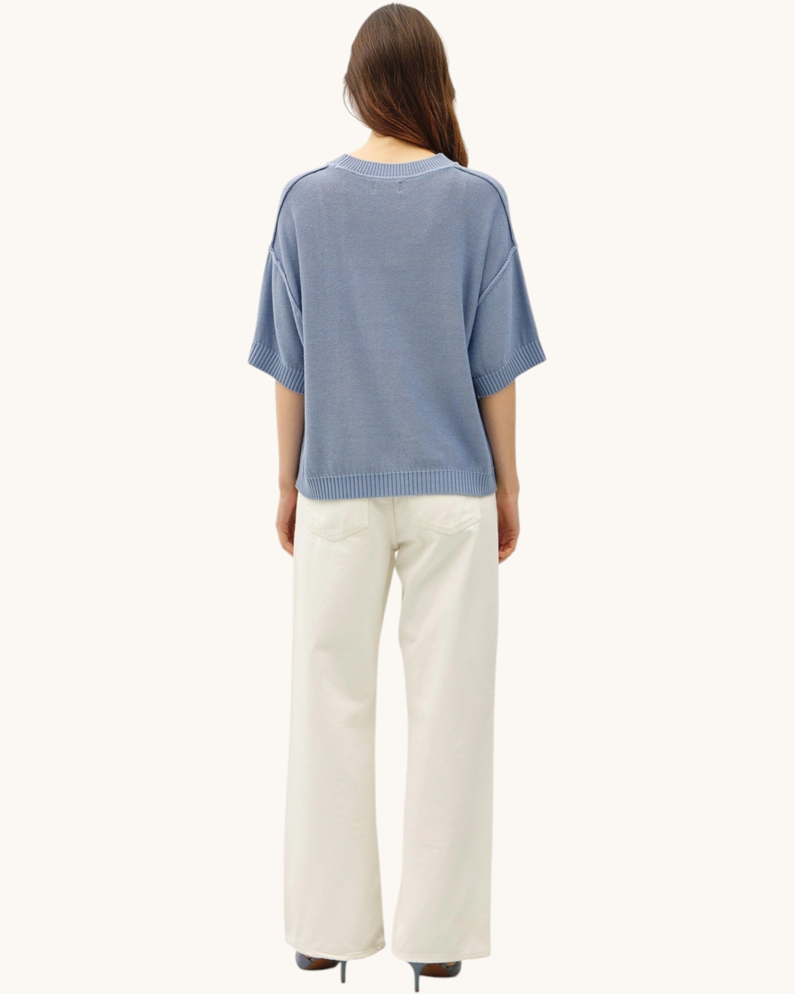Back view of a person wearing a blue sweater and white pants on a white background.