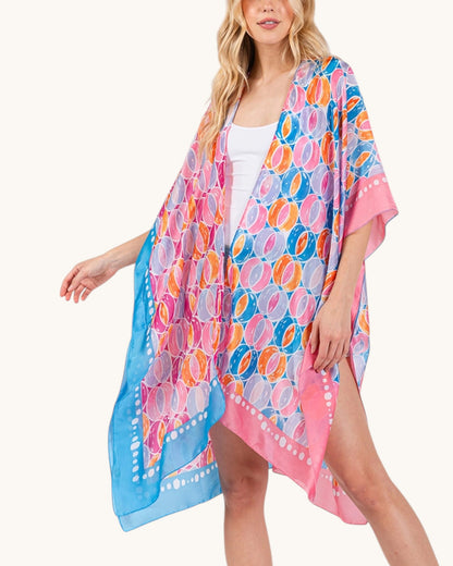 Woman wearing a colorful pink, blue and orange patterned cover-up on a white background.