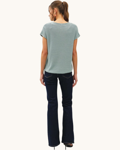 Back view of a woman wearing a blue short sleeve knitted top and dark denim jeans.