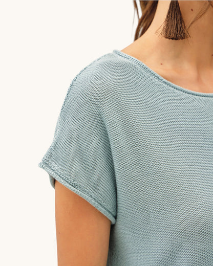 Close up of a light blue short sleeve knitted top worn by a person on a white background.