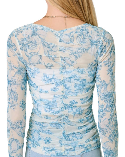 Woman wearing a white and blue floral long-sleeve top on a white background.
