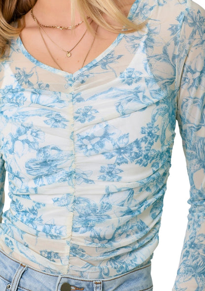 Woman wearing a white and blue floral long-sleeve top on a white background.
