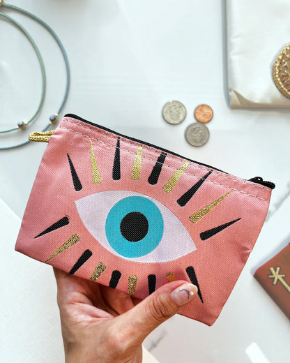 Pink pouch with eye design held by a hand on a white background.