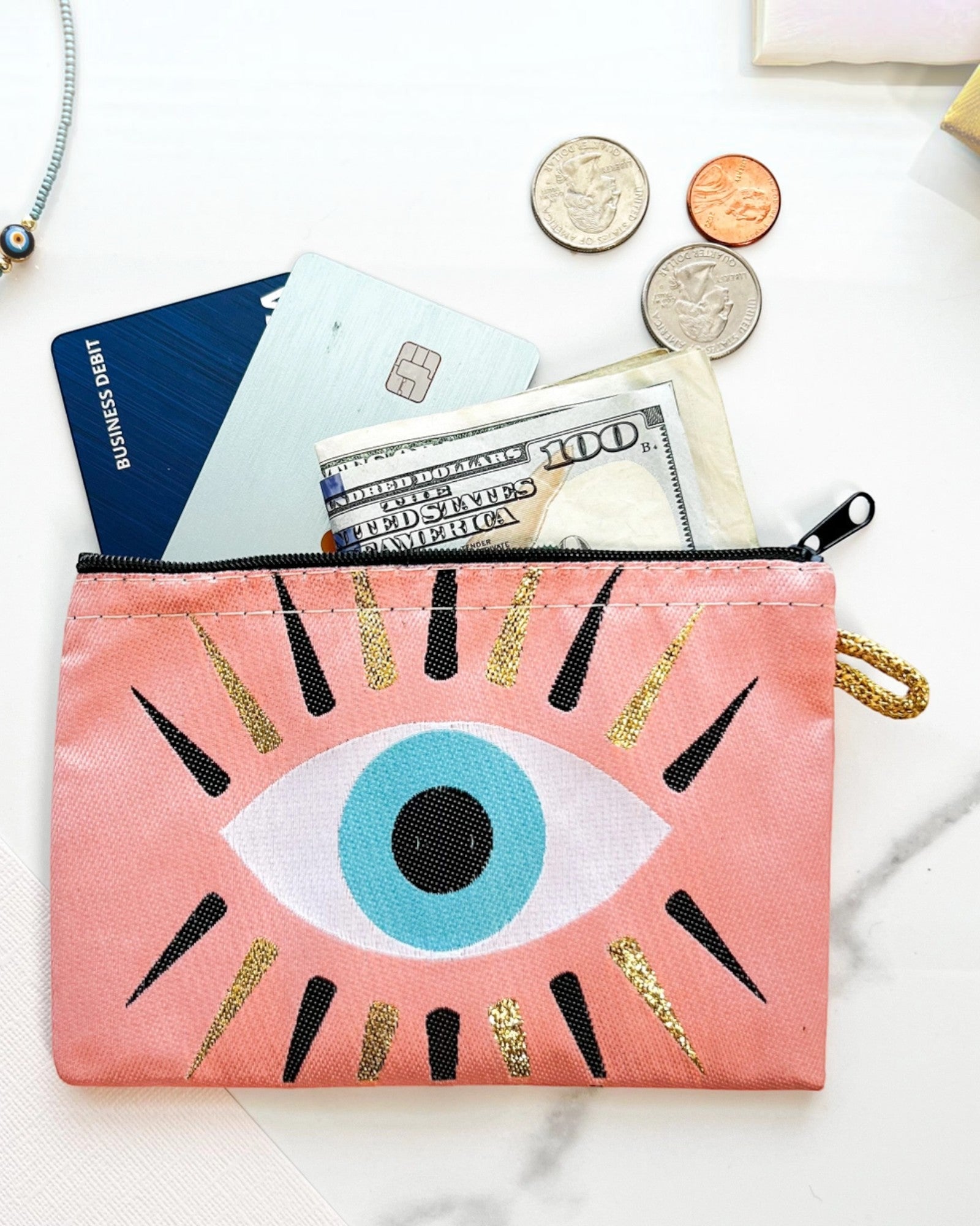 Pink pouch with evil eye design containing money and cards on a white background.