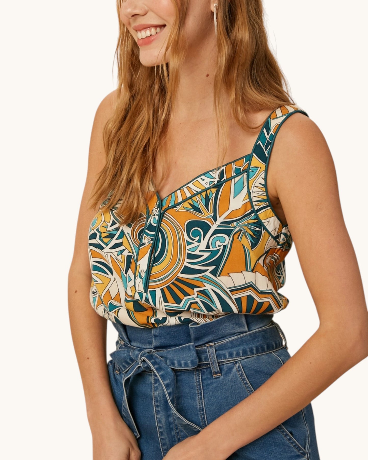 Woman wearing a patterned boho top and blue jeans on a white background.
