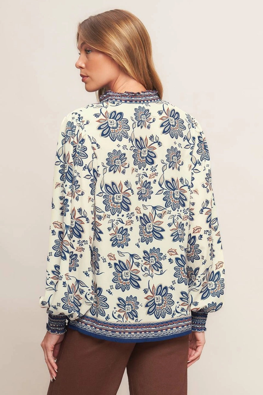Ivory navy border print blouse with ruffled V neckline and smocked cuffs.