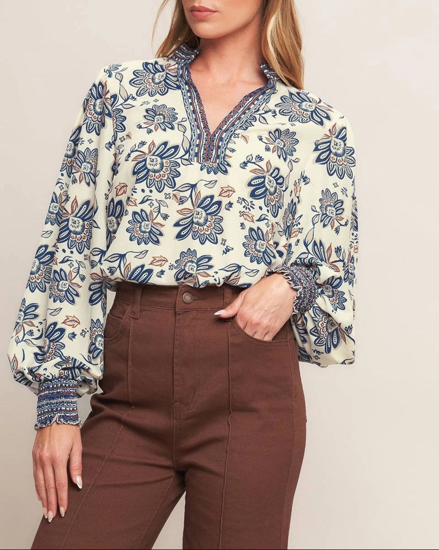 Ivory navy border print blouse with ruffled V neckline and smocked cuffs.