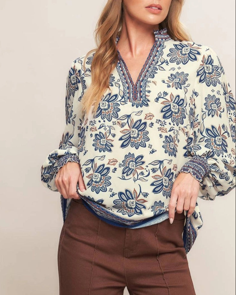Ivory navy border print blouse with ruffled V neckline and smocked cuffs.
