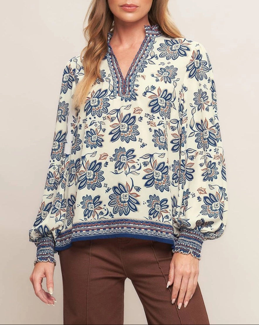 Ivory navy border print blouse with ruffled V neckline and smocked cuffs.